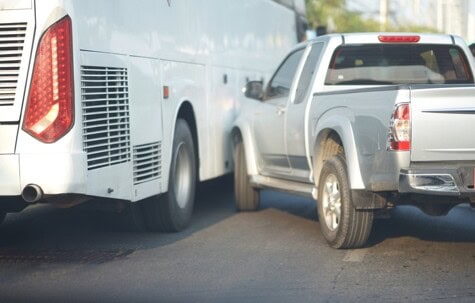 A silver pickup truck is in close contact with a white bus on a street.