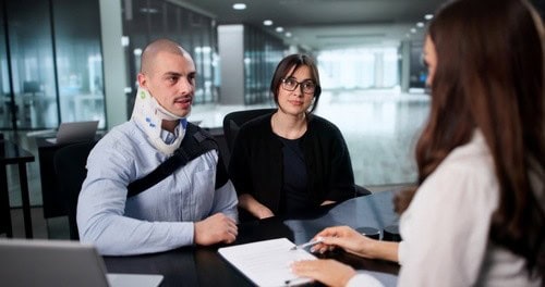 Man wearing neck brace seated with woman across desk during office consultation
